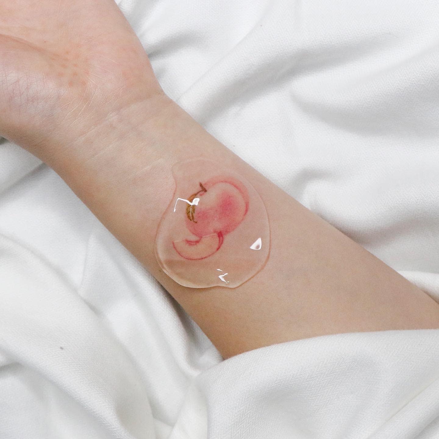 Soft, delicate watercolor-style tattoo of a peach on the wrist, covered with a protective film